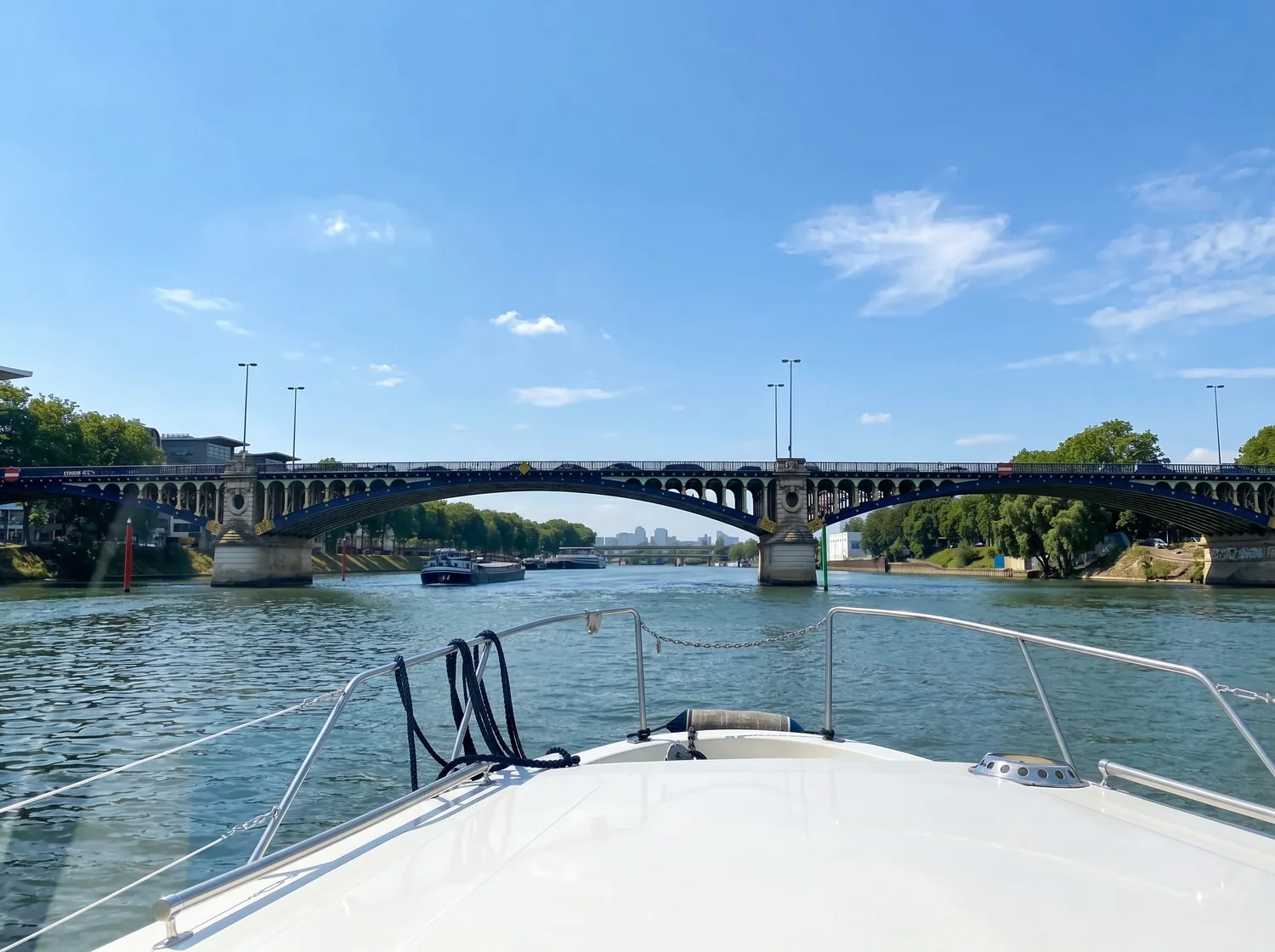 Vue depuis la proue du bateau blanc vers un pont de la Marne, ciel d'été bleu